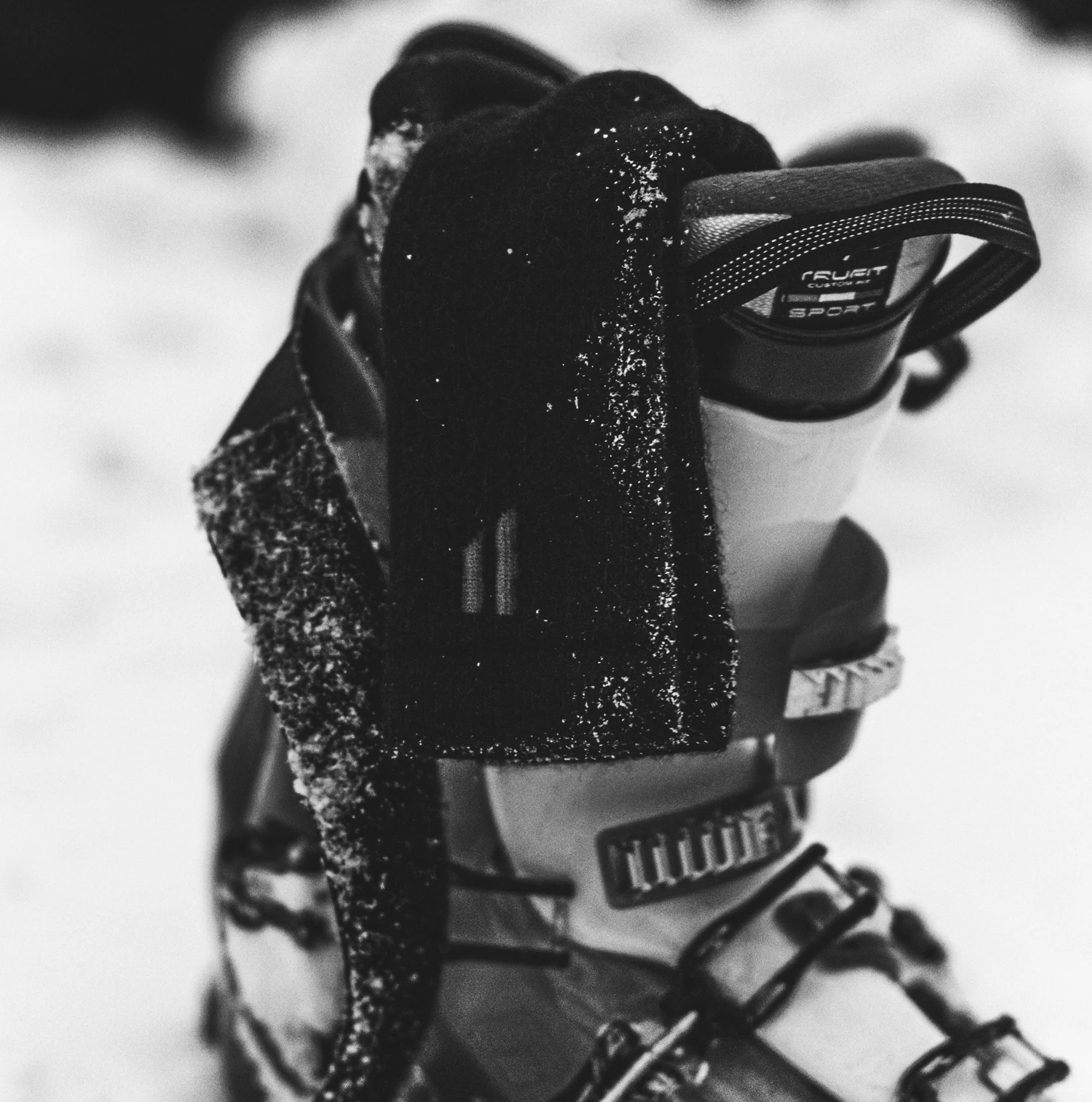 A black and white close-up photo of the top of a ski boot covered in snow.