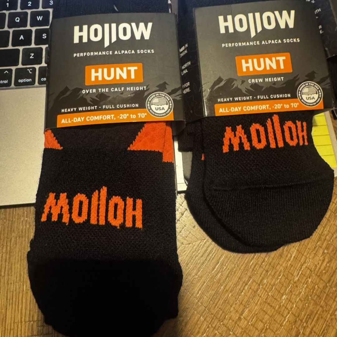 Two pairs of black and orange Hollow performance alpaca socks in their packaging on a wooden surface.