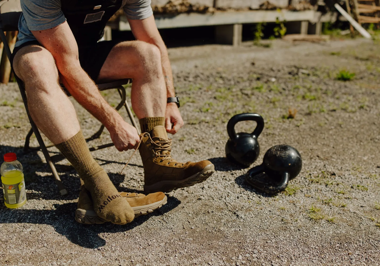 A person sits on a chair outdoors and ties the laces of a tan boot.