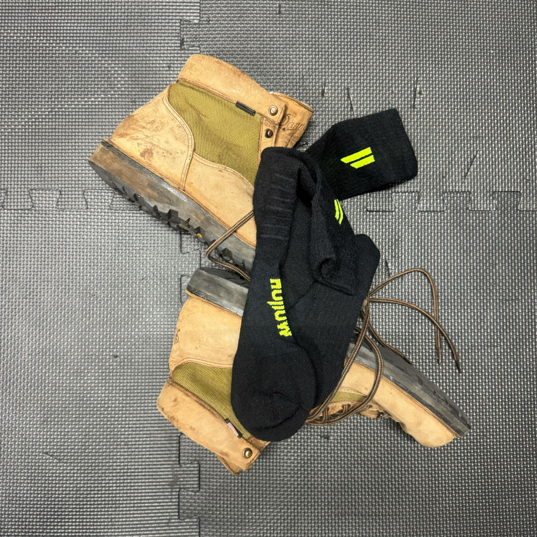 A pair of tan work boots and black socks with yellow accents on a textured gray floor.