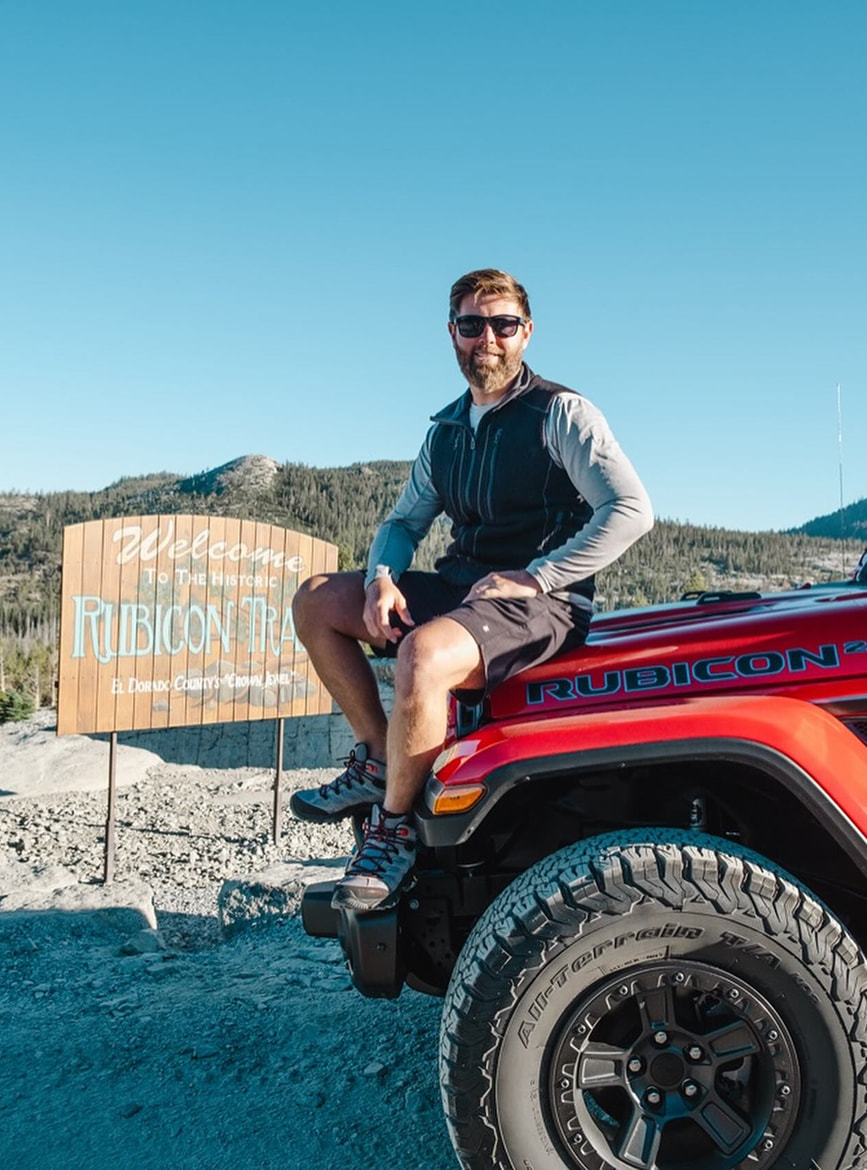 Man sitting on a red Jeep near Rubicon Trail sign.