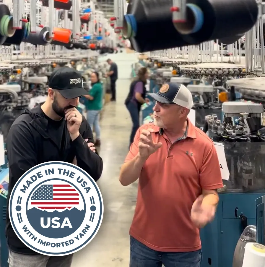 Two men talking in a textile factory setting, with machines and threads visible.