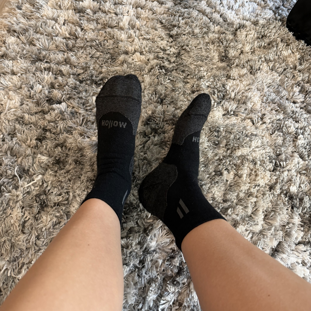 A first-person view of feet in black socks resting on a grey shag rug.