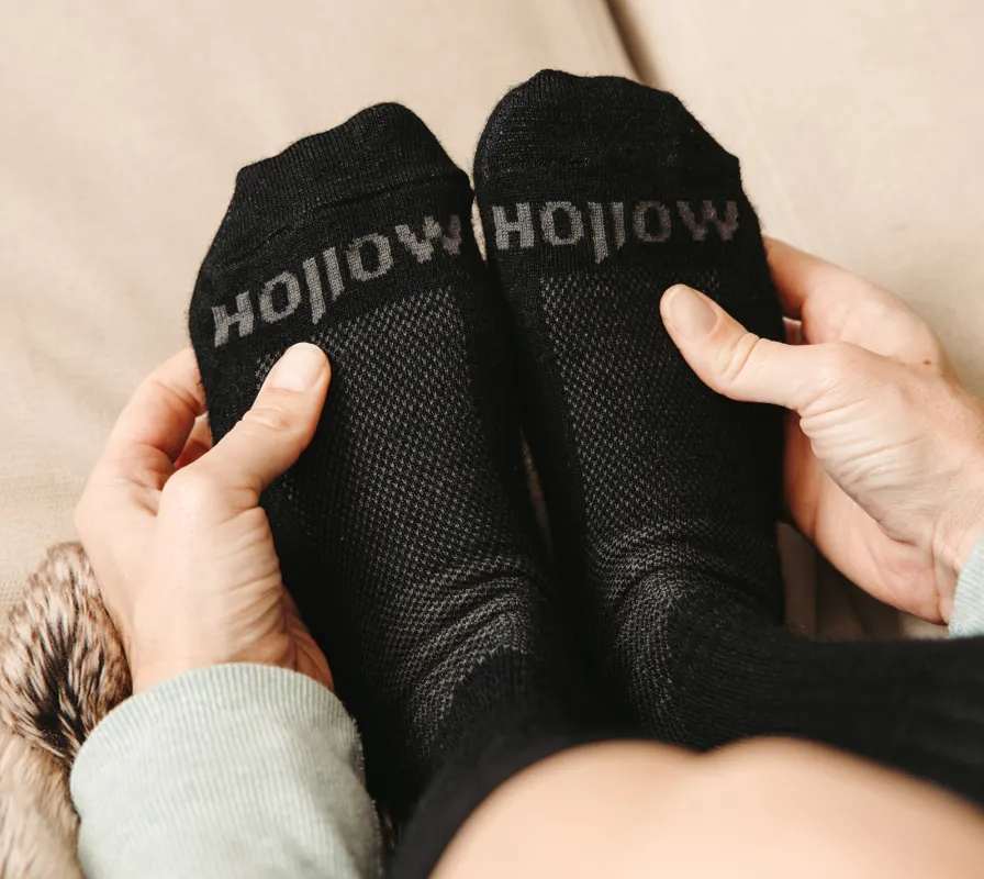 A person holds their feet, which are wearing black socks with the word 'hollow' on them.