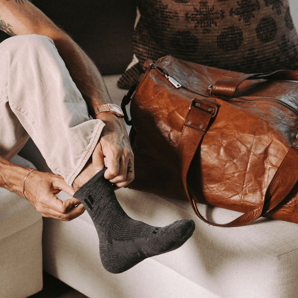 Man sitting next to leather bag wearing ankle socks