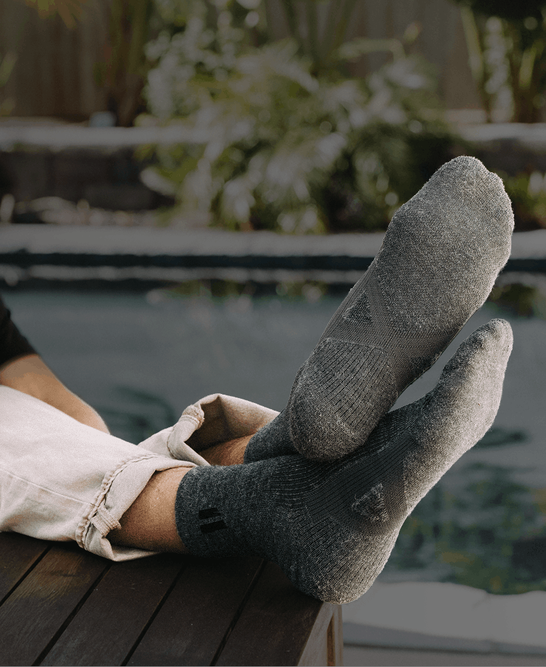 A person wearing grey socks relaxes with their feet propped up on a wooden surface outdoors.