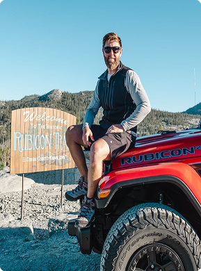 Person sitting on a red Jeep near a Rubicon Trail sign.