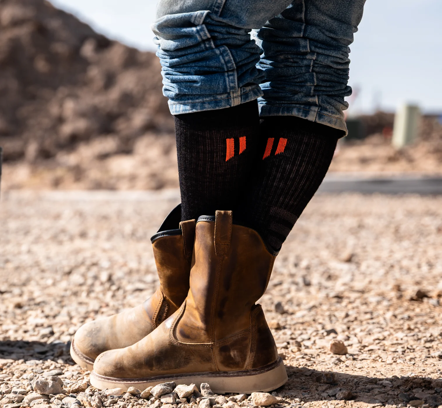 Person wearing brown boots and rolled-up jeans standing on gravel.