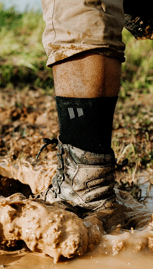 A muddy boot stepping in a puddle of mud on grassy terrain.