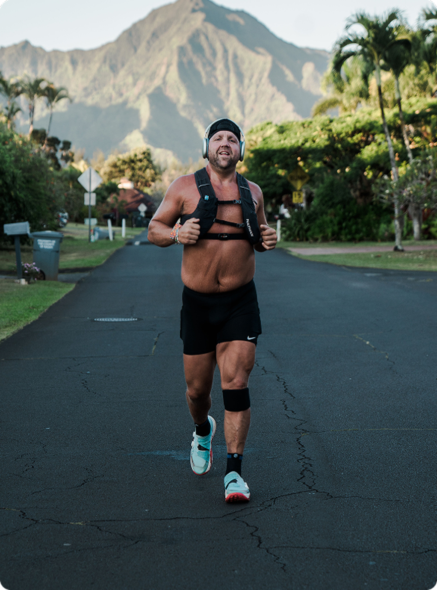 Man jogging on a road with mountains and palm trees in the background.