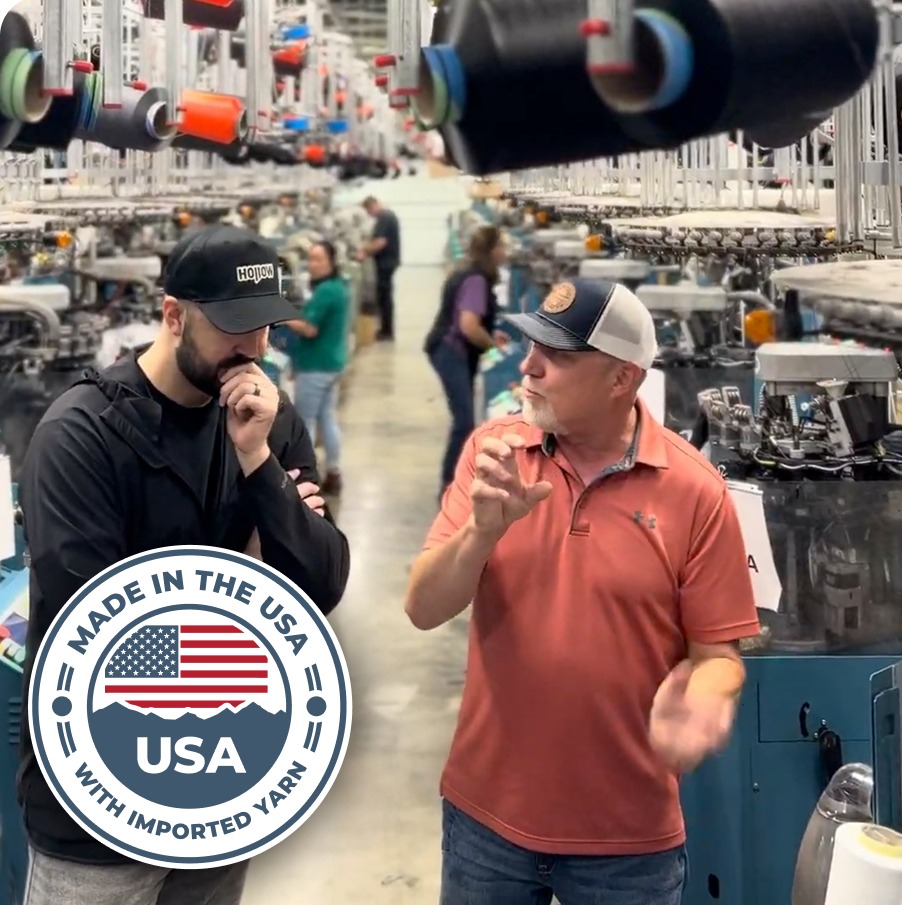 Two men talking in a textile factory with machinery and yarn spools.
