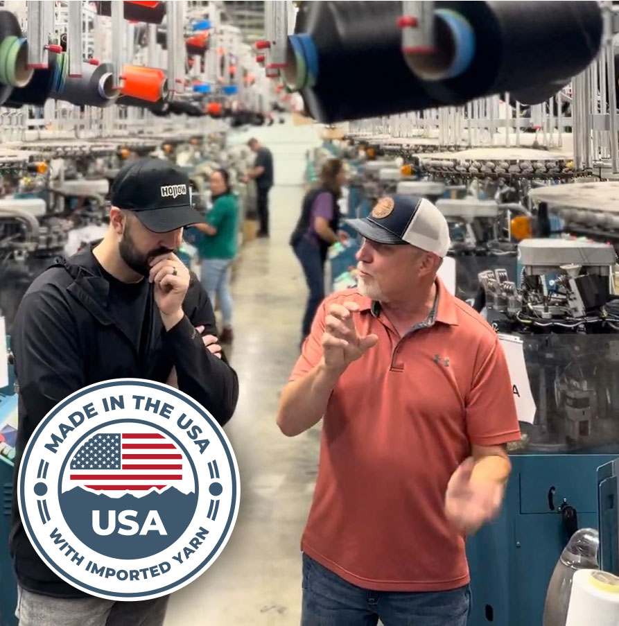 Two men talking in a textile factory with machinery and spools of yarn.