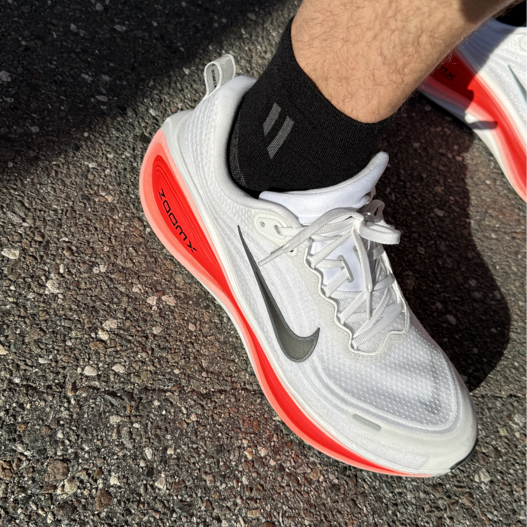 A close-up of a person wearing a white and red Nike ZoomX running shoe on asphalt.