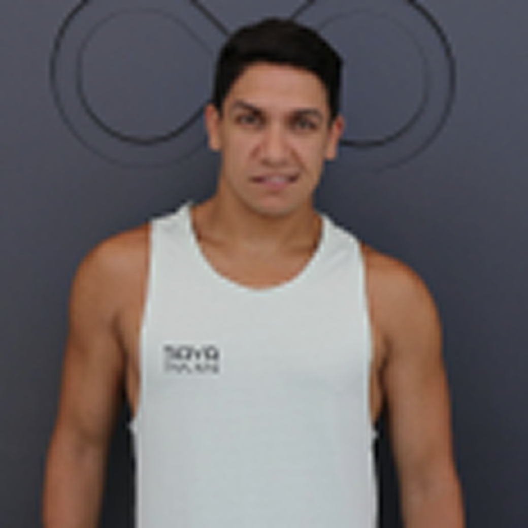 A man with short dark hair, wearing a white tank top, looks towards the camera against a gray background.