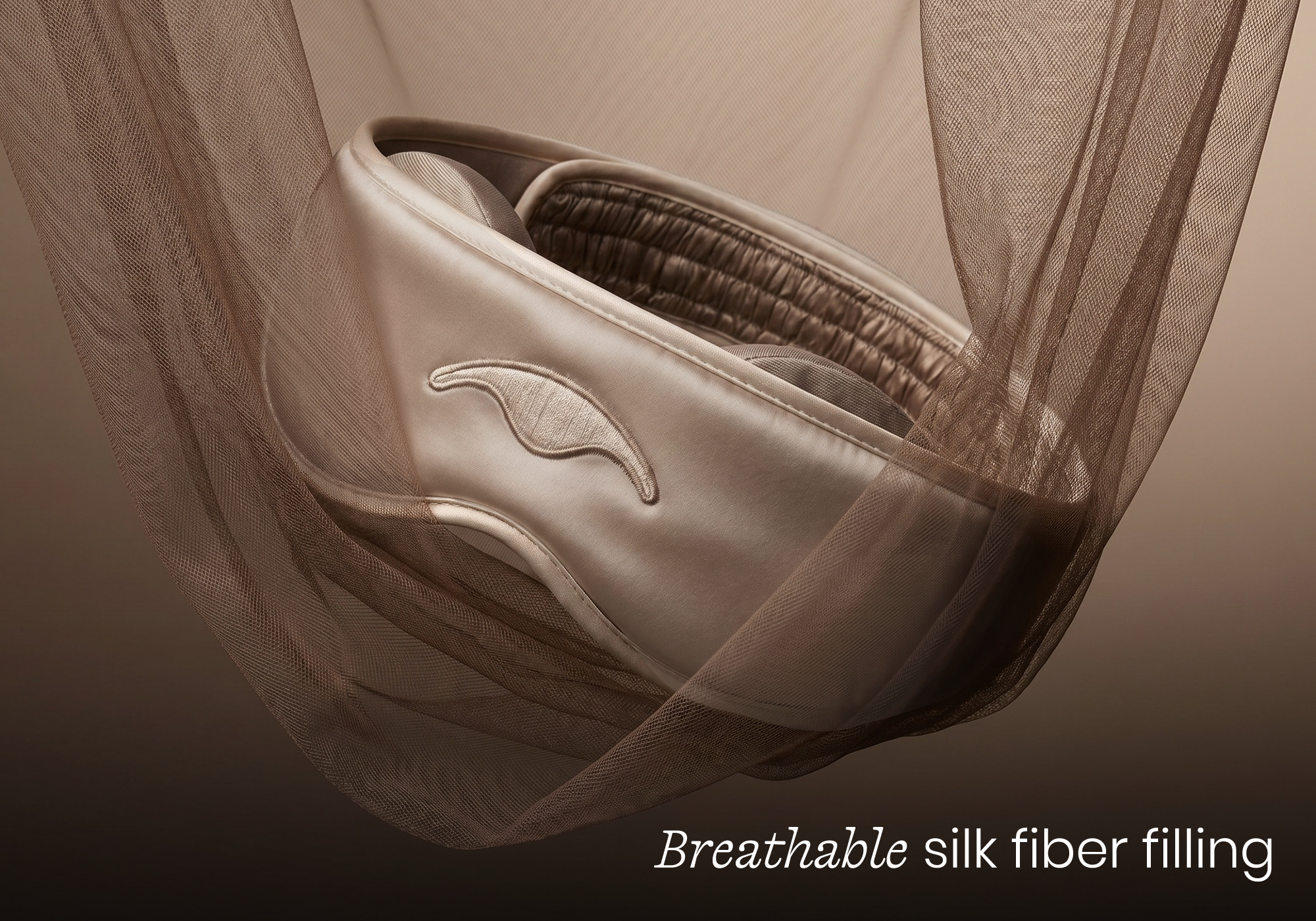 A champagne-colored satin eye mask is cradled within a piece of sheer, brown mesh fabric.