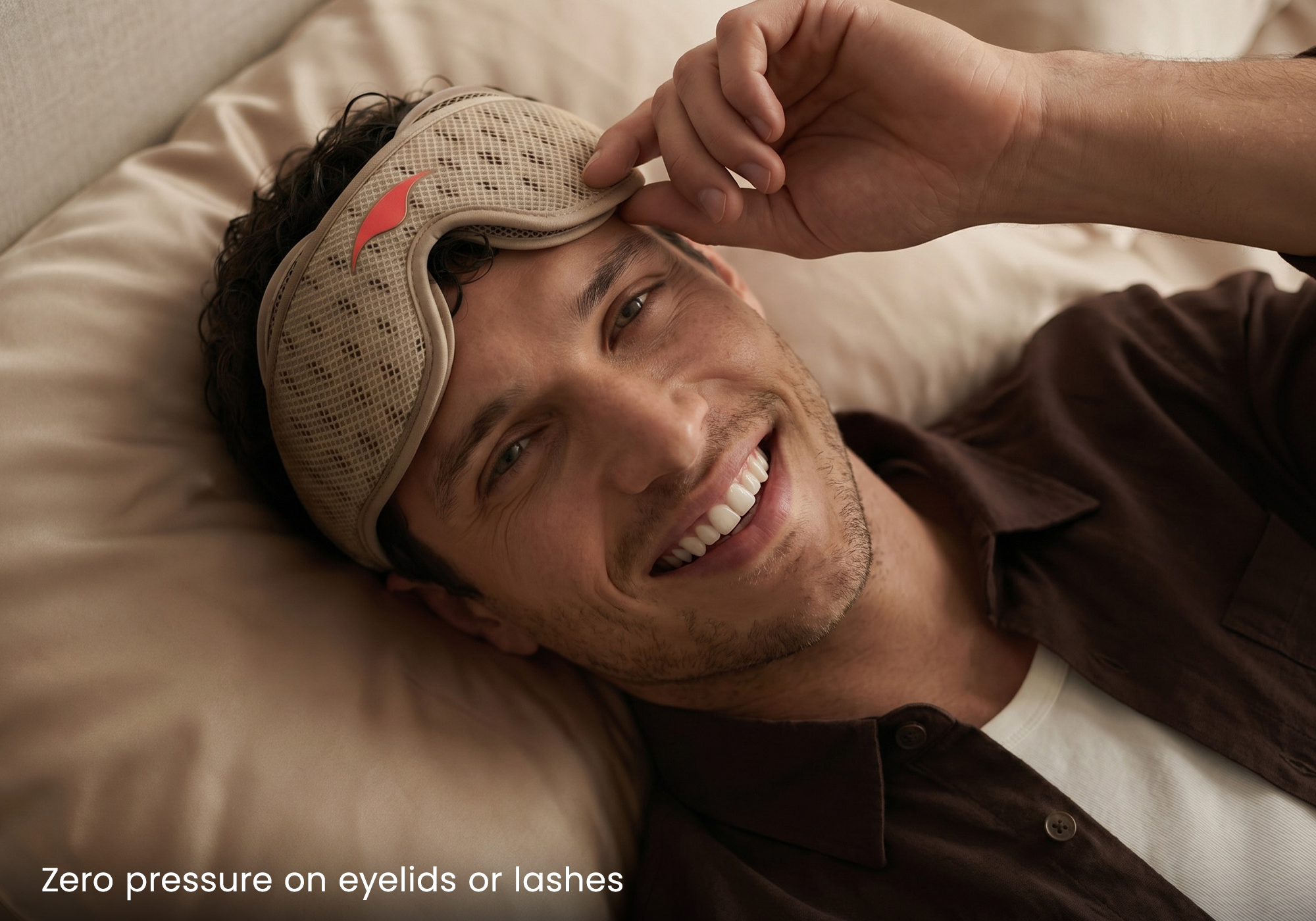 Image of smiling man laying down in bed wearing a cream and brown Manta Sleep mask.