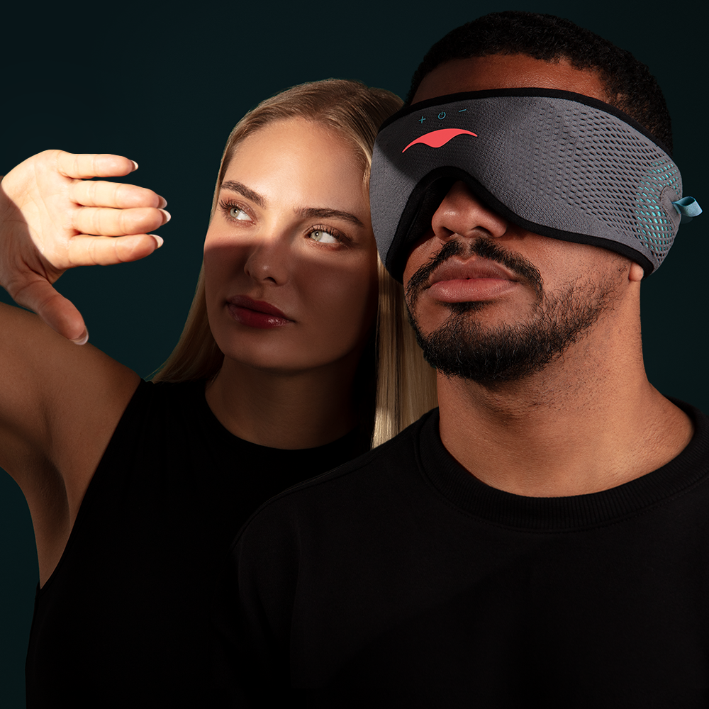 A man wearing a gray electronic sleep mask, with a woman behind him shielding her face from light.
