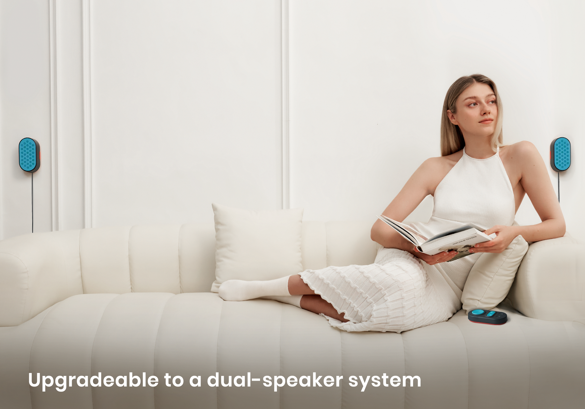 Woman in white dress reading on a white sofa with blue speakers on the wall.