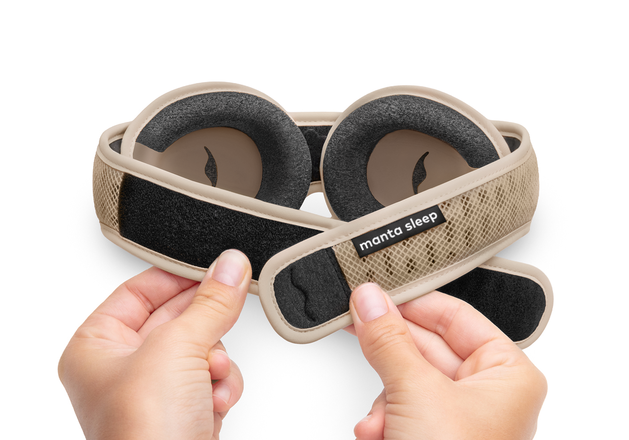 A person's hands adjusting the velcro strap on a tan-colored Manta Sleep mask against a white background.