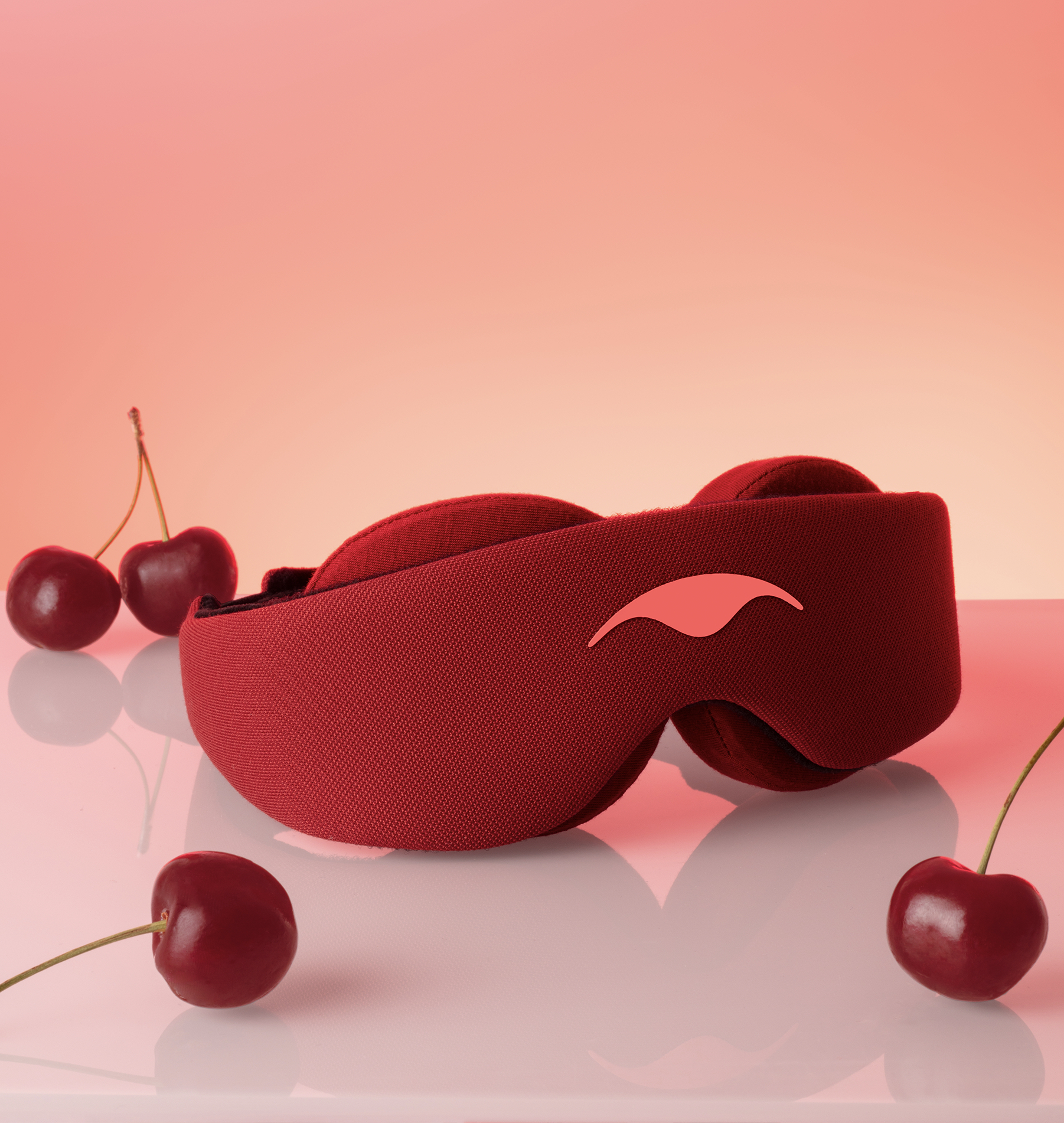 Red sleep mask on a reflective surface with cherries around it.