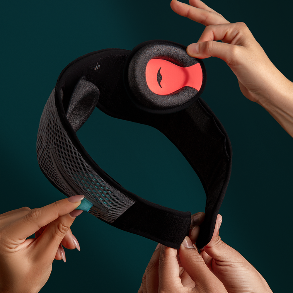 Several hands hold and adjust a black padded headband with a red circular earpiece against a dark background.