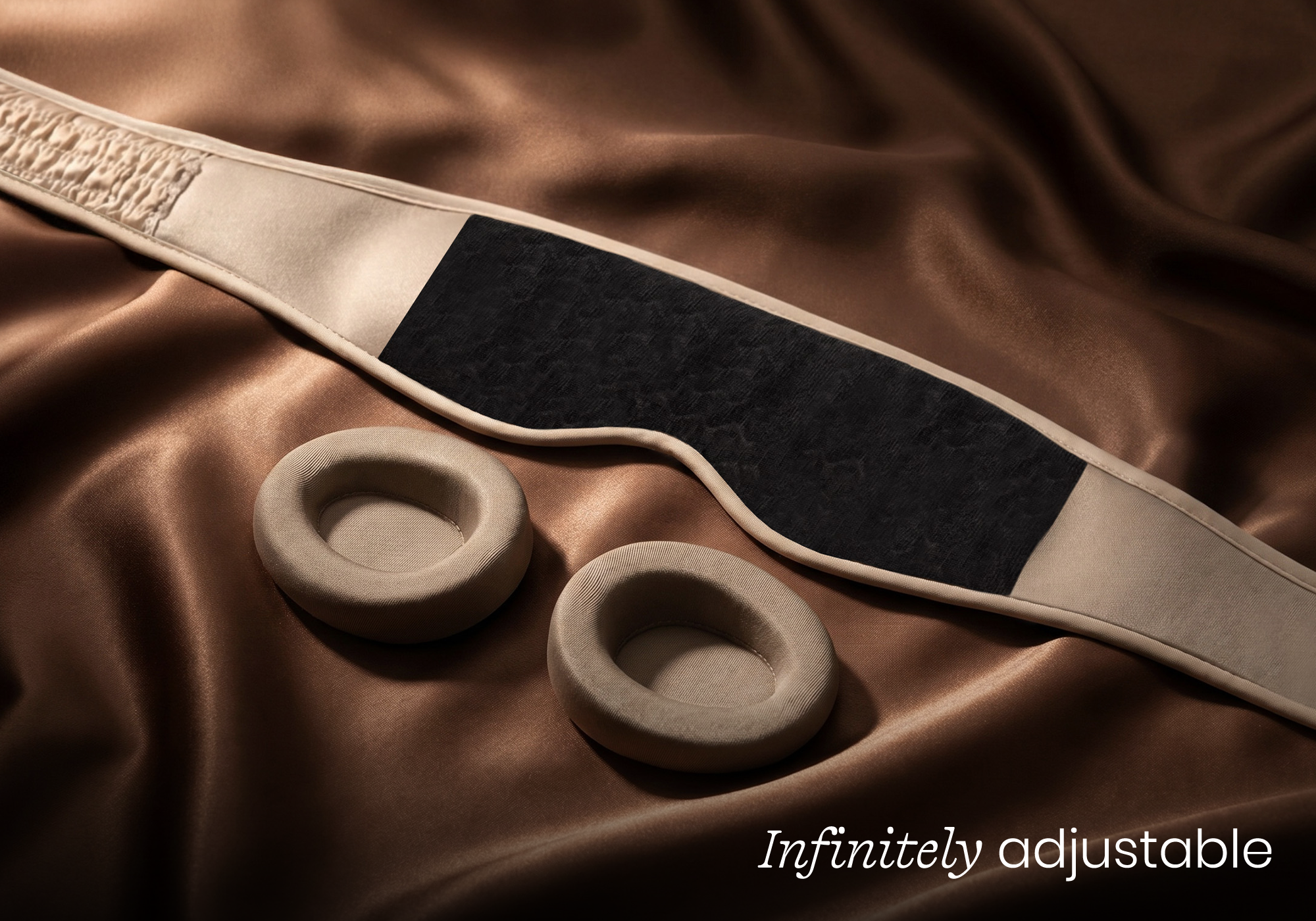 A beige sleep mask with its two separate eye cups resting on a brown silk cloth.