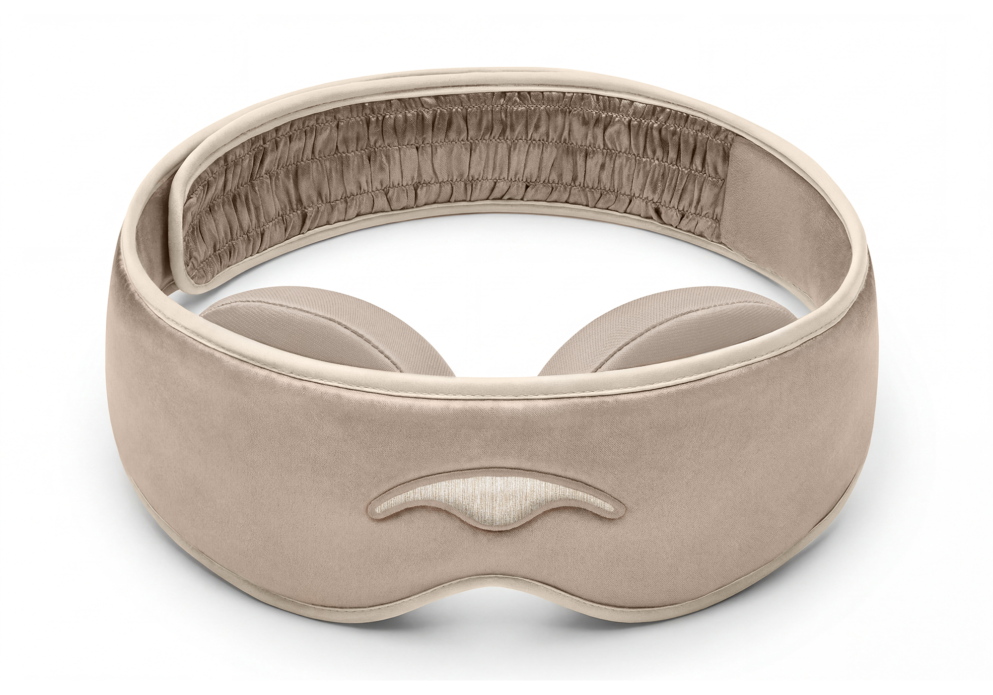 A soft, beige eye mask with padded eye cups and a ruched elastic strap against a white background.