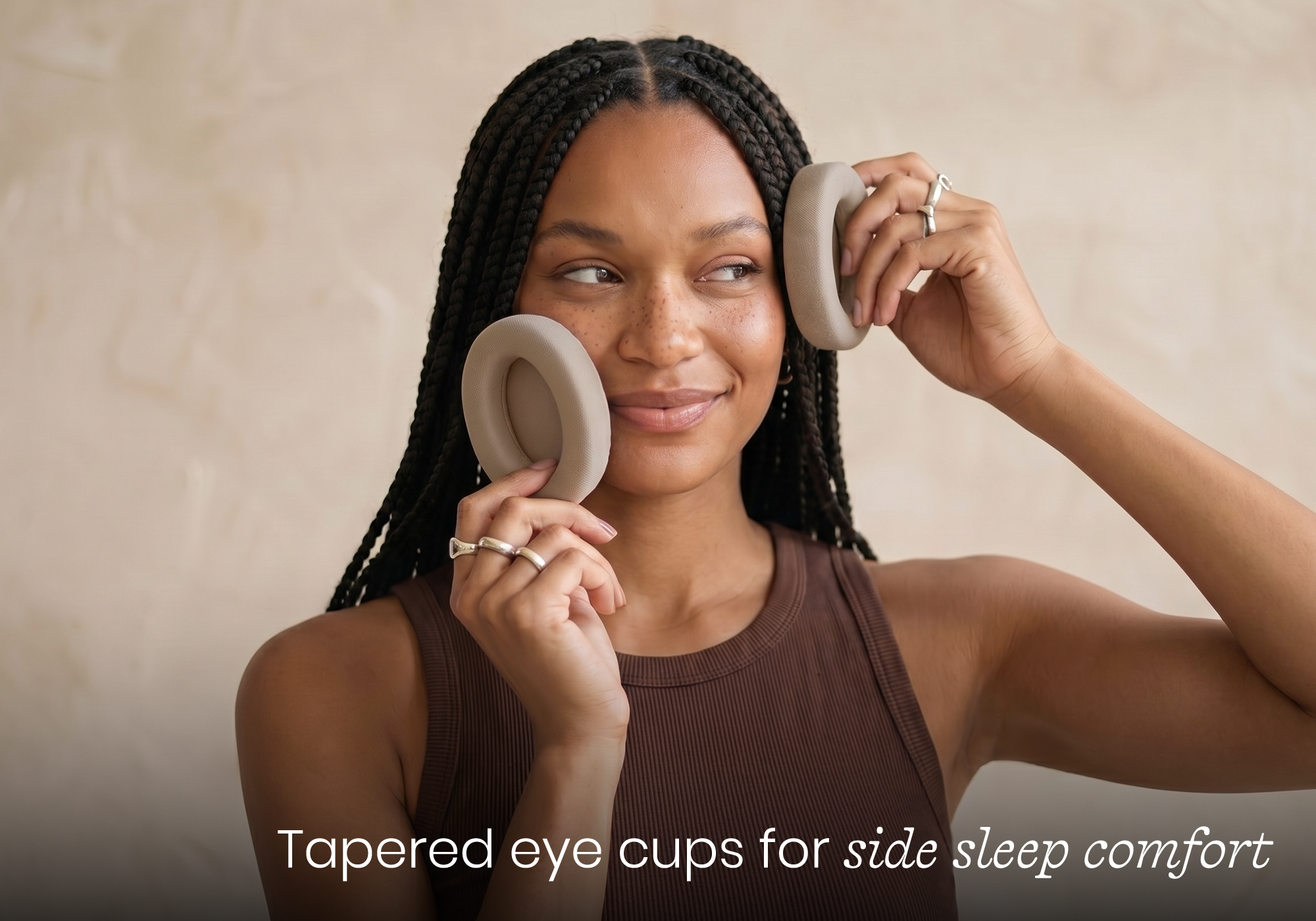 A smiling woman with braided hair holds two soft, gray, tapered eye cups to her cheeks.