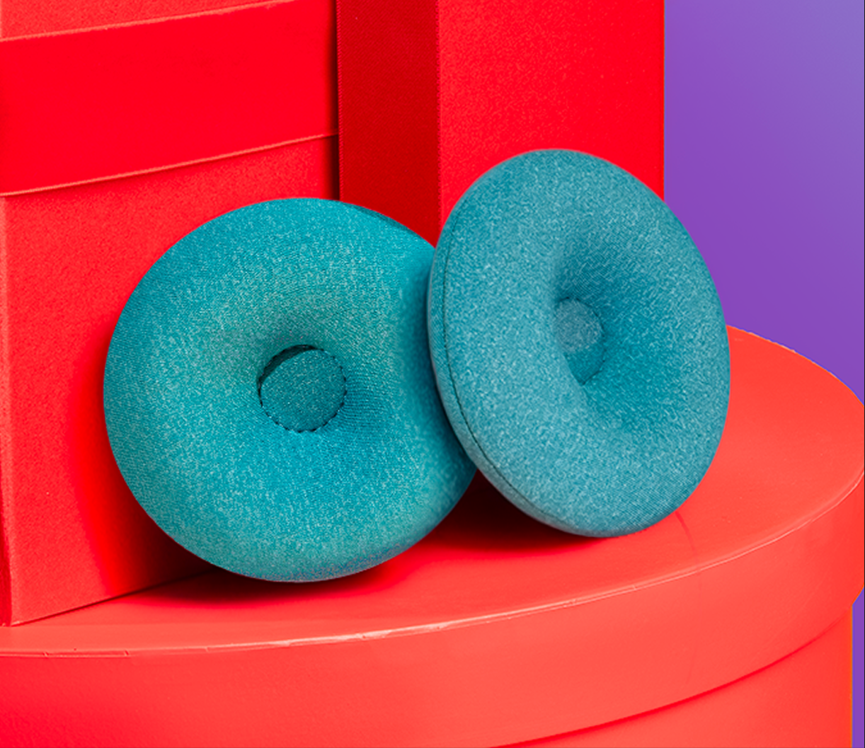 Two turquoise foam donuts on red boxes and purple background.