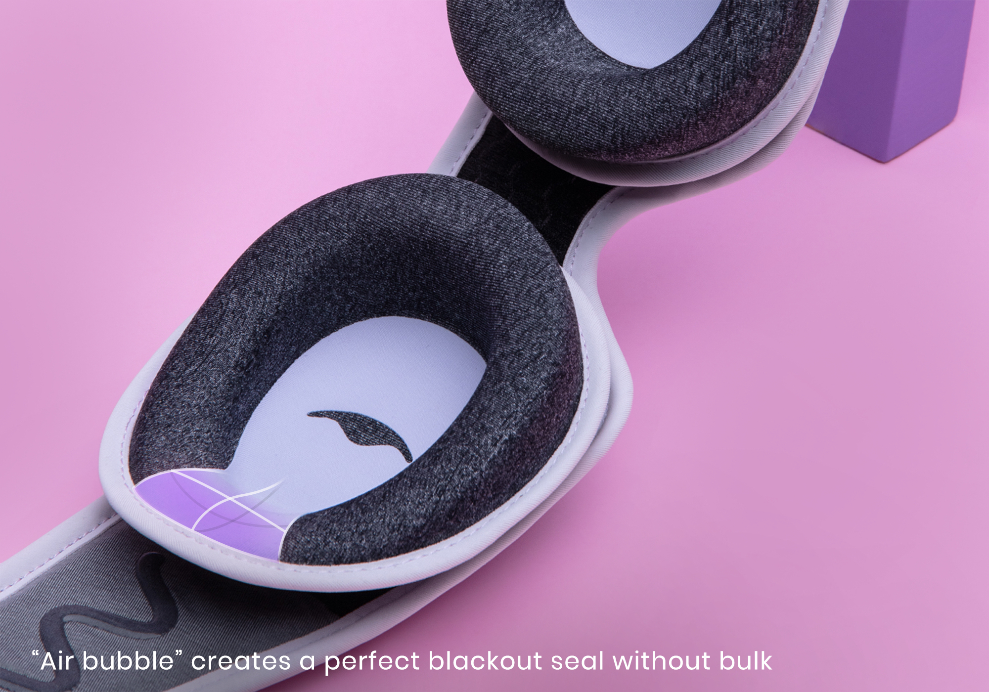 Black sleep mask with comfortable padding on a pink background.