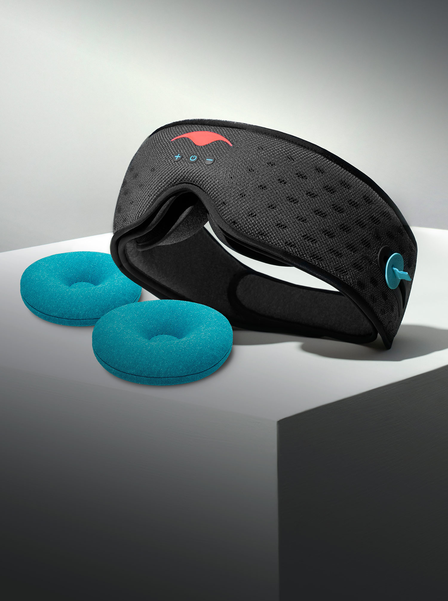 Black sleep mask with buttons and two blue cushions on a white surface.