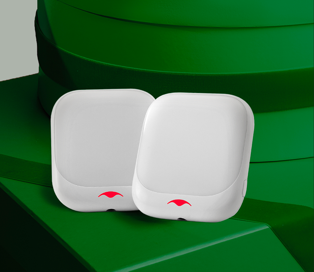 Two white square devices with a red logo on a green surface.