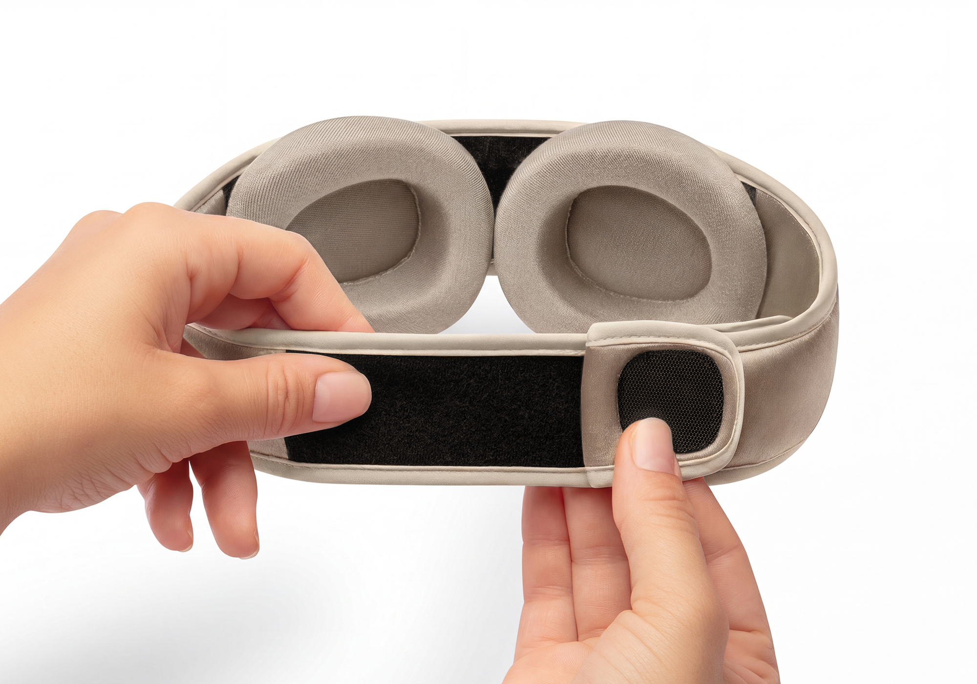 A person's hands adjusting the velcro strap on the back of a padded, beige eye mask.