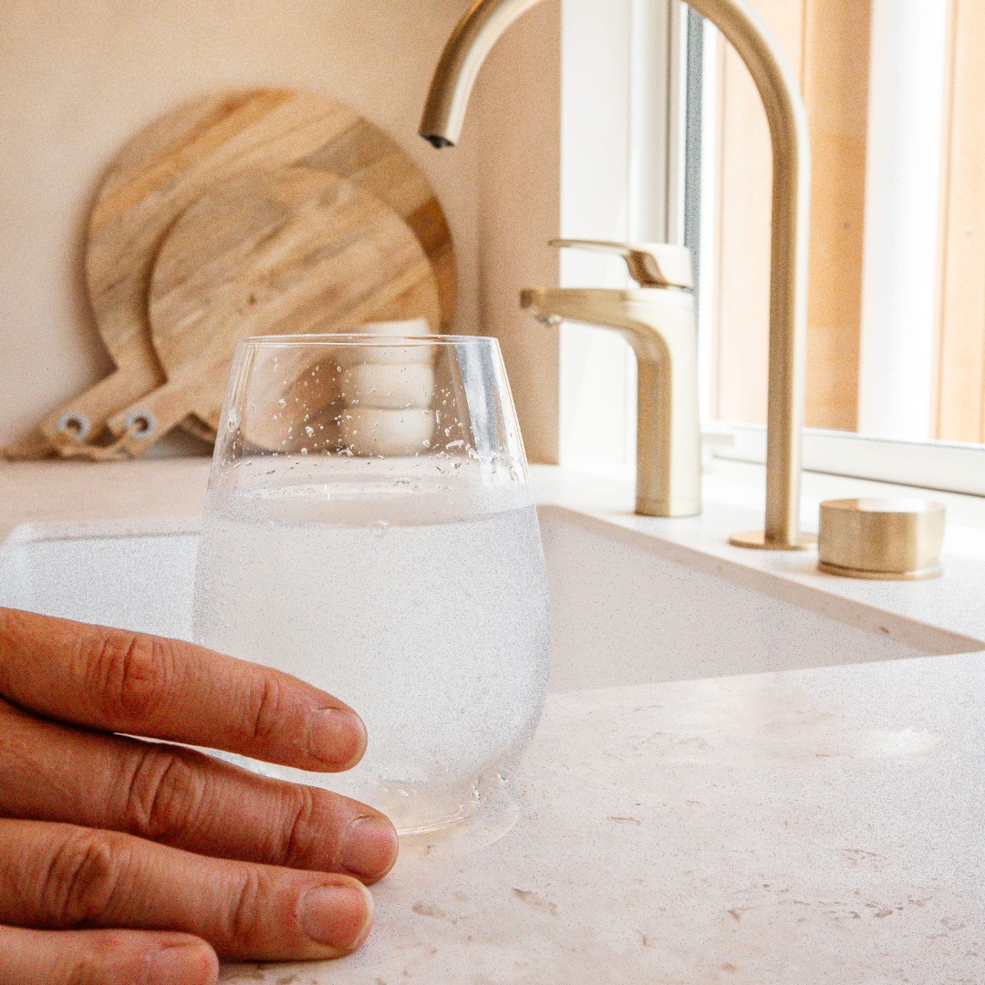 Hand holding a glass of water by a kitchen sink.