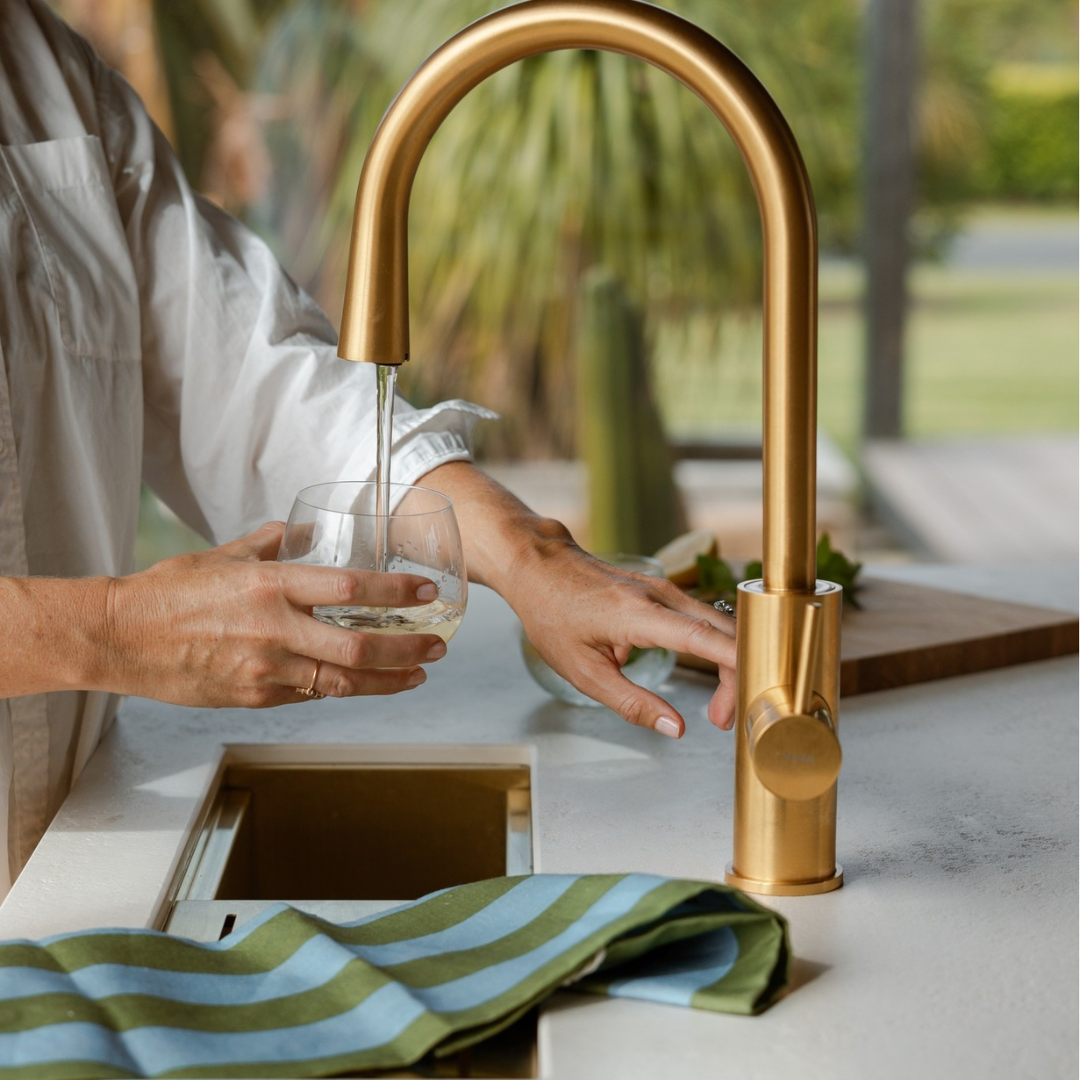 Modern kitchen faucet with running water and a steaming cup on the counter.