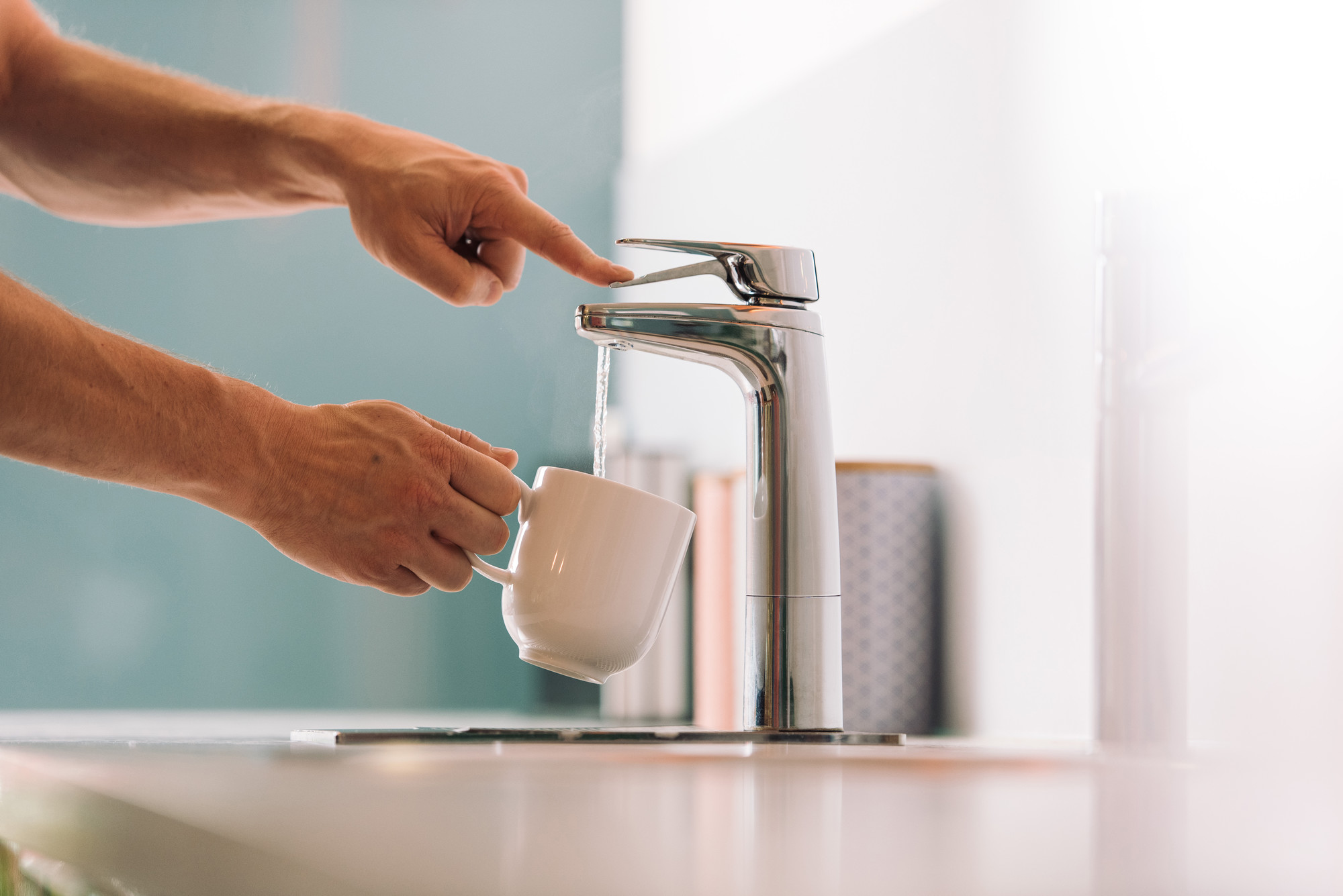 Person filling a white mug with water from a modern faucet.
