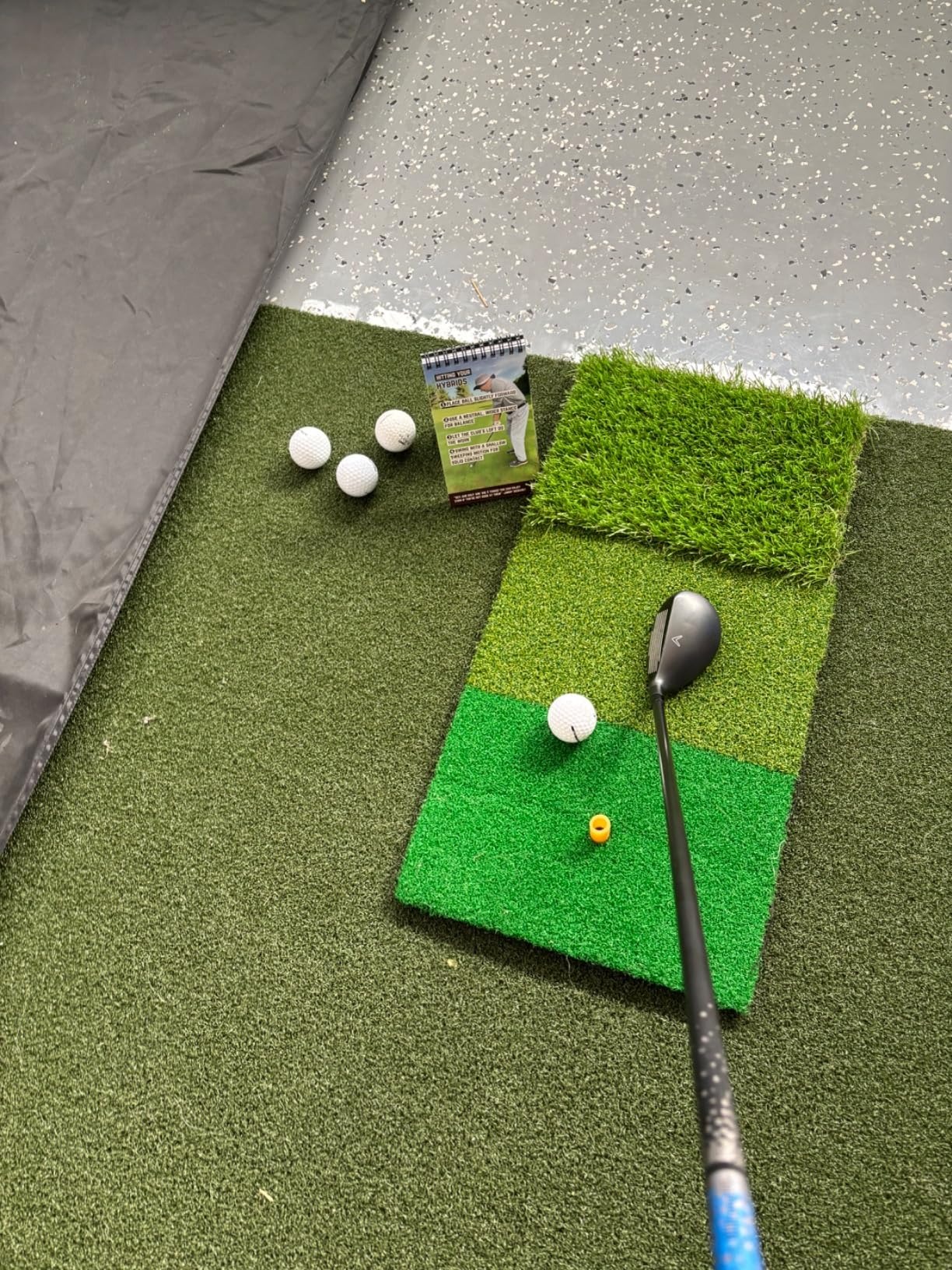 Golf club and balls on artificial turf with a practice guide.