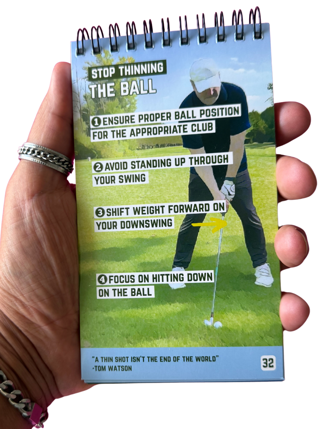 A hand holding a spiral-bound golf tip booklet open to a page titled 'Stop Thinning The Ball'.