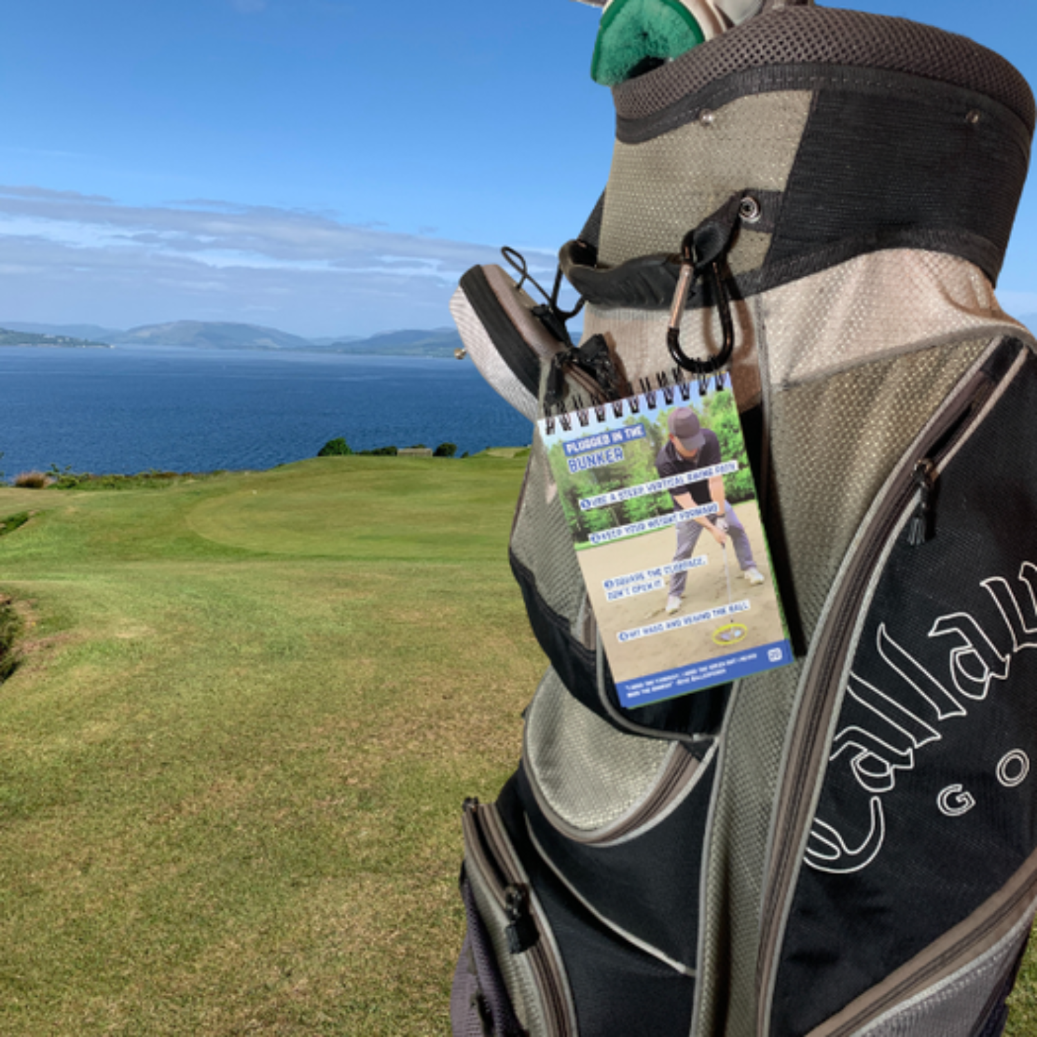 Golf bag on a course with ocean and hills in the background.