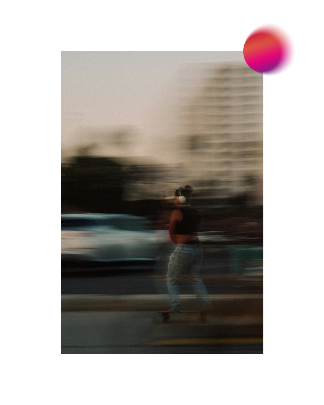A motion-blurred photo of a person from behind on a skateboard, wearing headphones on a city street.