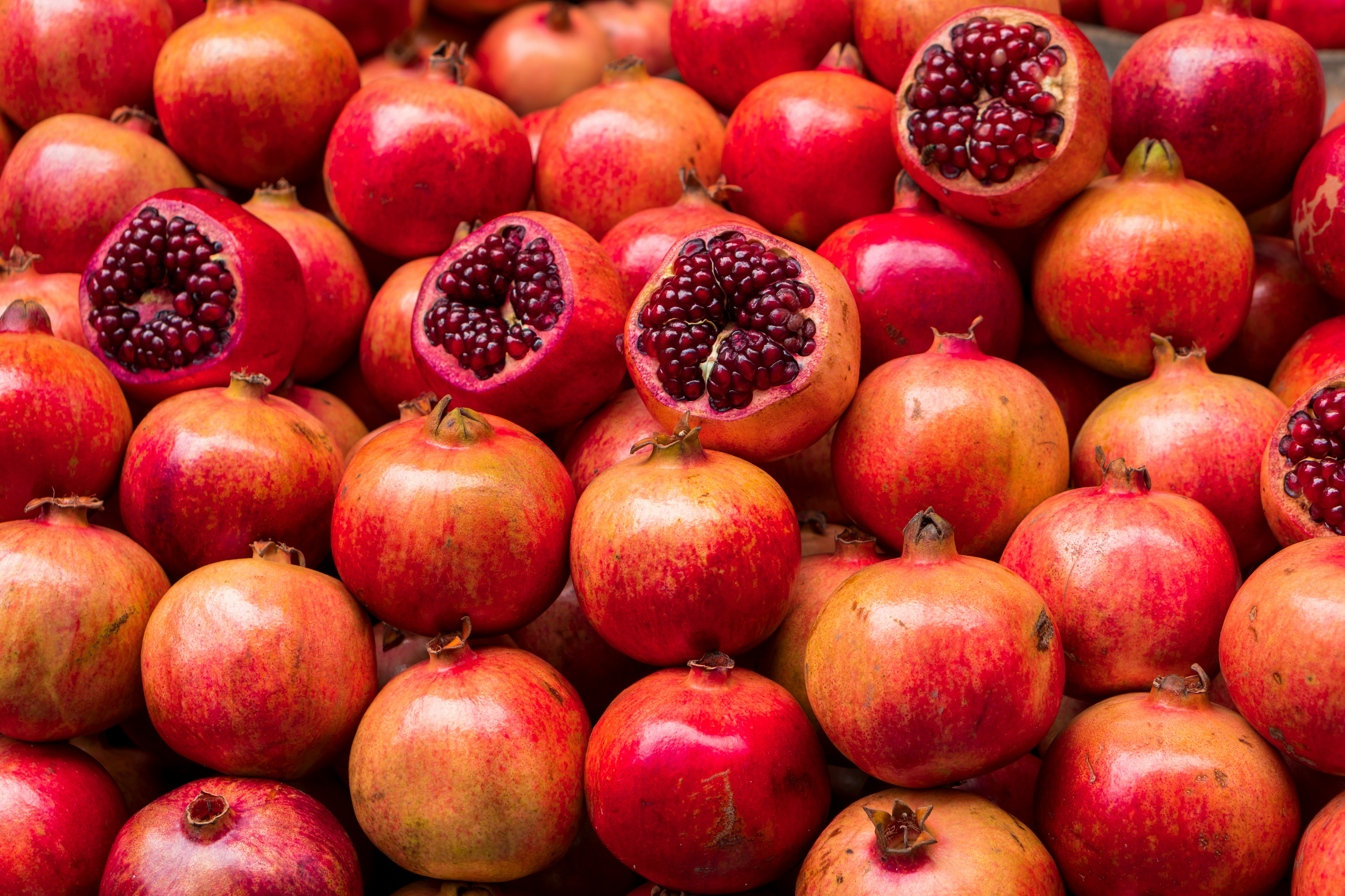 A pile of whole and halved pomegranates showing seeds.