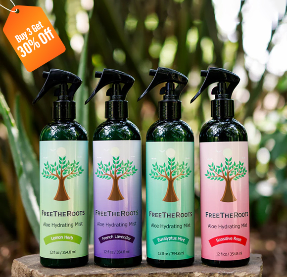 Four bottles of Free The Roots Aloe Hydrating Mist in different scents, displayed outdoors on a rock.