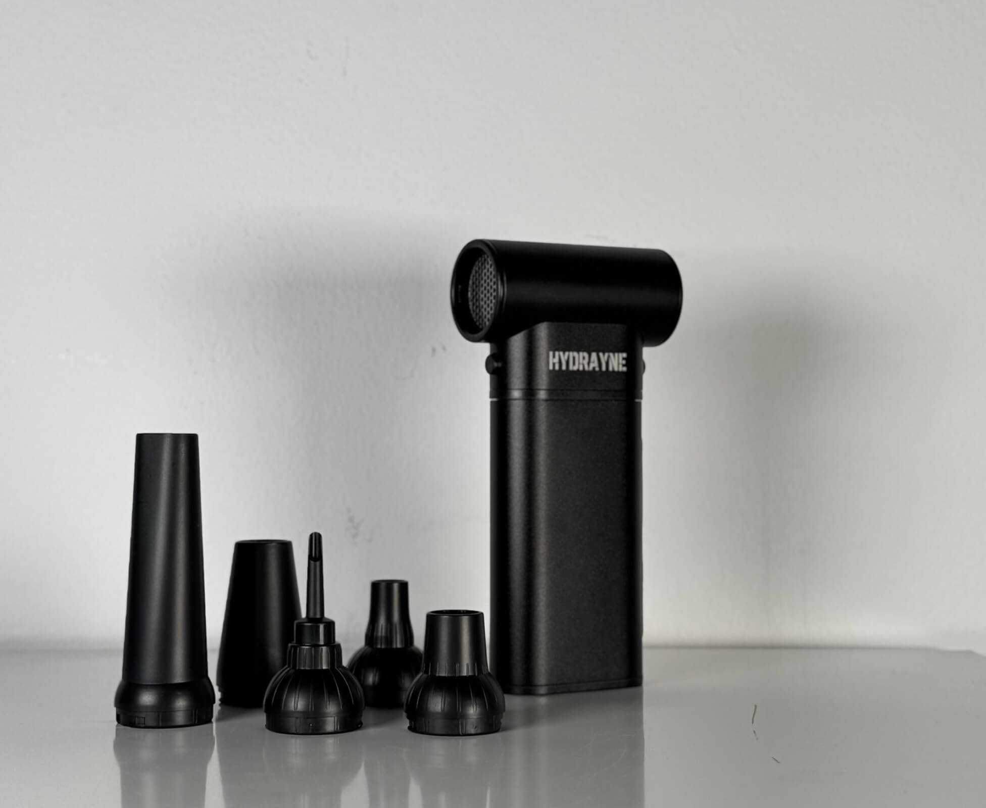 A black electric hair dryer, hair brush, and hair curler arranged together on a white background.