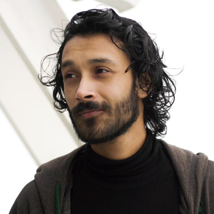 Person with dark hair and beard, wearing a black shirt and gray hoodie.