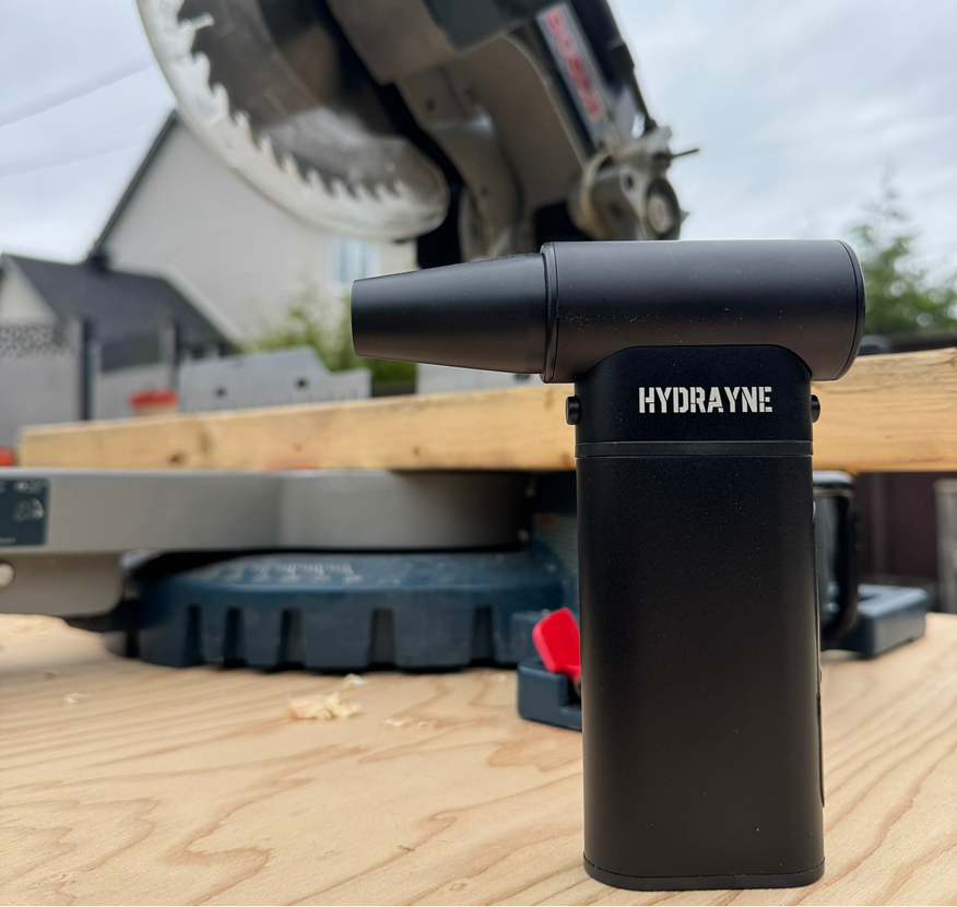 Black torch lighter on wooden surface with saw in background.