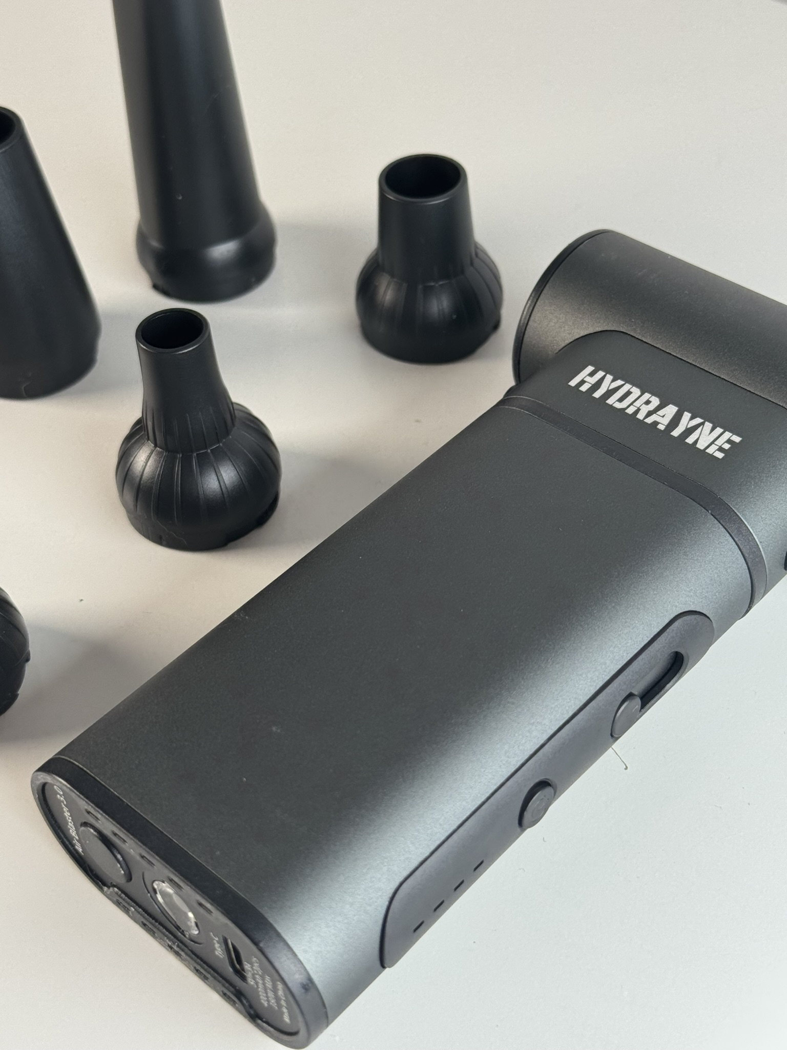 Black device with 'HYDRAYNE' label and multiple nozzle attachments on a white surface.