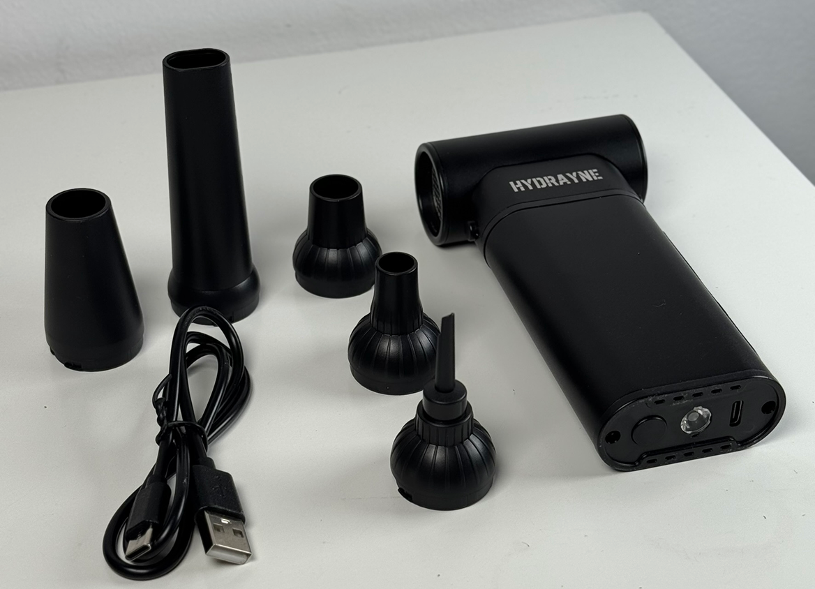 Black handheld device with multiple nozzle attachments and a USB cable on a white surface.