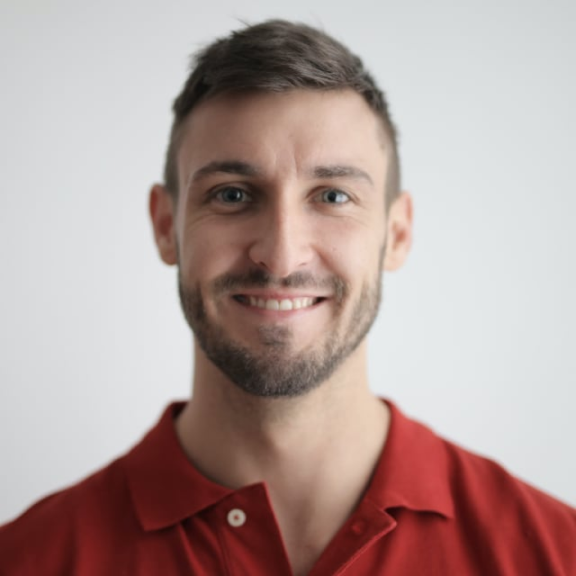 Smiling man in a red polo shirt against a plain background.