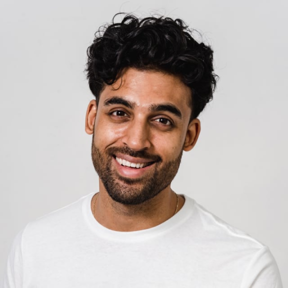Smiling man with curly hair wearing a white shirt against a plain background.
