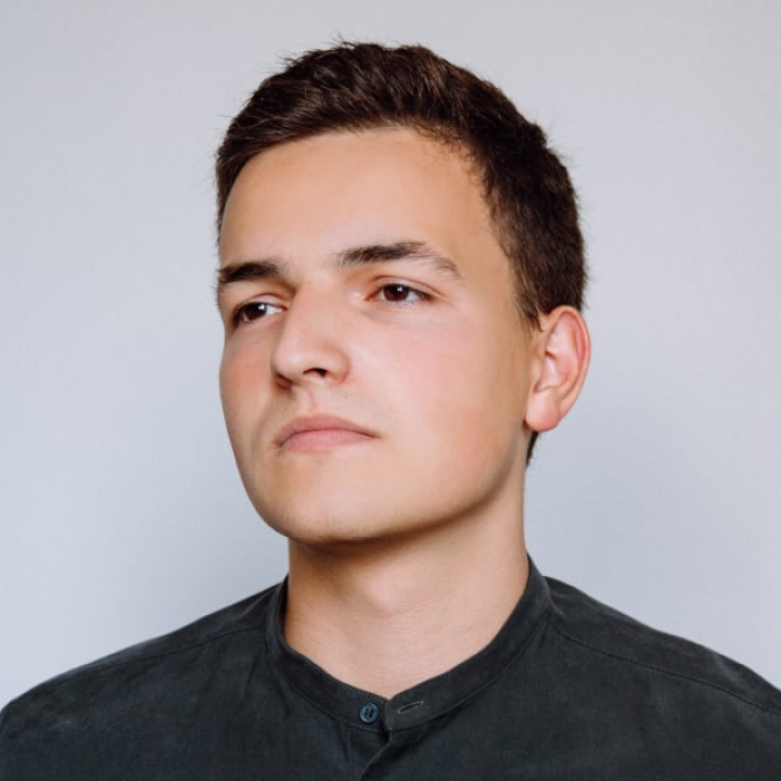 A person with short hair wearing a dark shirt, looking slightly to the side.